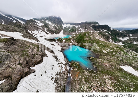 Aerial wide angle view of an alpine lake high in the mountains. Lake surrounded by mountain peaks partially covered with snow 117574029