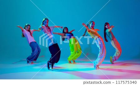 Dynamic synchronized movements of young girls, teens in motion, dancing hip hop against cyan blue background in neon background 117575340