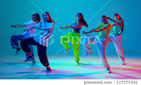 Group of young dancers, girls in dynamic motions, performing, dancing hip hop against cyan blue background in neon background 117575342