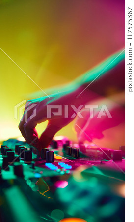 DJ, bathed in colorful light, creates electric atmosphere, his every move synchronized with beats that echo through space. 117575367