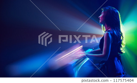 Symphony of light and sound. Pianist plays as waves of color fill space, her form silhouette against radiant glow that surrounds her. Symphony of light and sound. Pianist plays as waves of color fill space, her form silhouette against radiant glow that surrounds her. 117575404