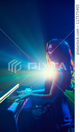 Pianist's music seems to paint air with colors of light that swirl around her, fusion of sound and vision. Woman playing piano on stage. 117575405