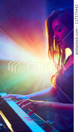 Close up photo of young woman playing piano solo on stage in dynamic, vibrant spotlights. Creative occupation. 117575442