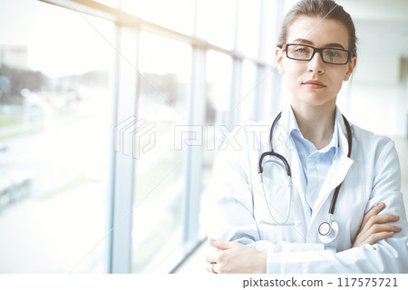 Beautiful woman doctor with stethoscope smiling charmingly and ready to help patients in sunny hospital. Medicine concept 117575721