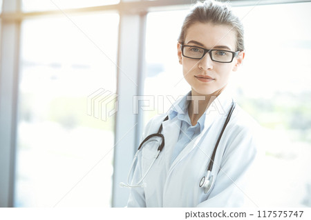 Beautiful woman doctor with stethoscope smiling charmingly and ready to help patients in sunny hospital. Medicine concept Beautiful woman doctor with stethoscope smiling charmingly and ready to help patients in sunny hospital. Medicine concept 117575747