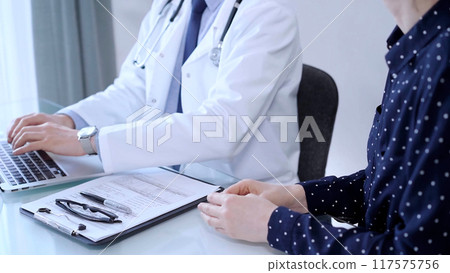 Doctor and patient are talking in clinic after health exam. Male physician is using laptop and discussing test results with a senior woman. Medicine concept 117575756