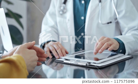 Doctor and patient consultation in clinic. Patient woman is gesturing over a glass desk while a physician is using tablet computer making some notes, close up of hands. Medicine and health care 117575896