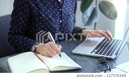 Businesswoman professional writing in a notebook beside a laptop at a modern workplace, close up view. Business concept 117576169