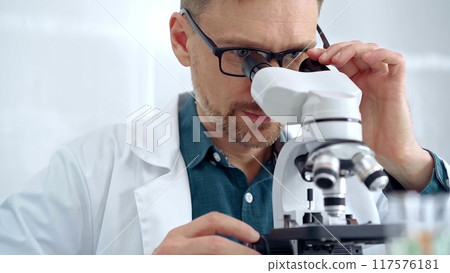 Man scientist with protective glasses using microscope in laboratory. Microbiology science concept 117576181