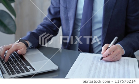 Businessman analyzing financial data on laptop and calculator. Close-up of a professional auditor working on financial reports. Business concept Businessman analyzing financial data on laptop and calculator. Close-up of a professional auditor working on financial reports. Business concept 117576214