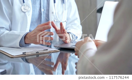 Doctor man and woman patient are discussing something and gesturing with their hands over a glass desk in medical office, close up. Medicine and Health care 117576244
