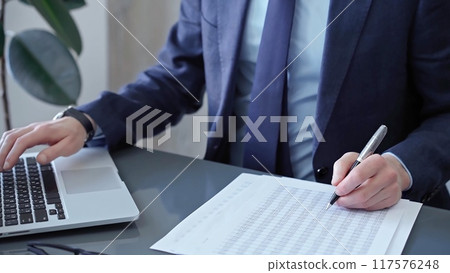 Businessman analyzing financial data on laptop and calculator. Close-up of a professional auditor working on financial reports. Business concept Businessman analyzing financial data on laptop and calculator. Close-up of a professional auditor working on financial reports. Business concept 117576248