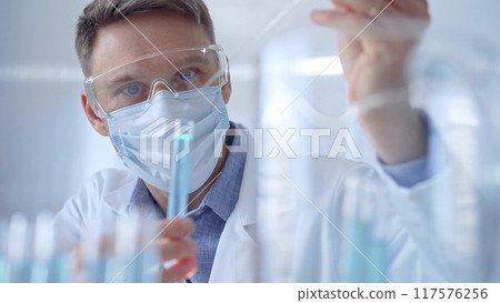 Man with safety glasses and blue mask is working with lab tubes Man with safety glasses and blue mask is working with lab tubes 117576256