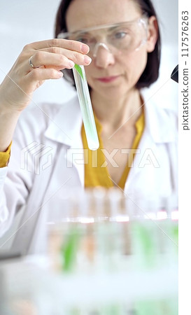 Scientist examining lab tube with a green fluid. Microbiology and science concept Scientist examining lab tube with a green fluid. Microbiology and science concept 117576263