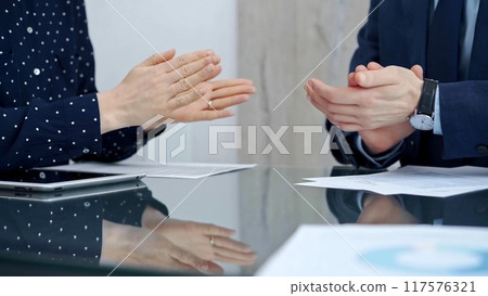 Unrecognizable business people shaking hands and clapping over glass table after contract signing in office. Agreement and handshake themes 117576321