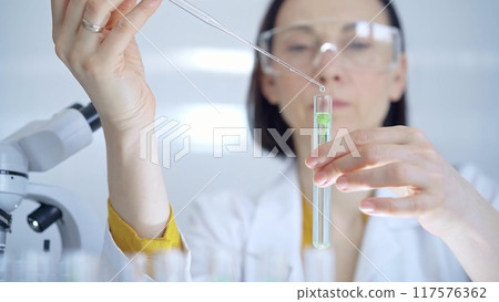 Woman with safety glasses is working with lab tubes using a pipe Woman with safety glasses is working with lab tubes using a pipe 117576362