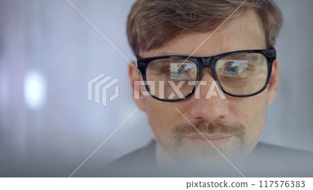 Businessman with glasses looking intently obscured partially by a translucent surface of laptop. Business concept Businessman with glasses looking intently obscured partially by a translucent surface of laptop. Business concept 117576383