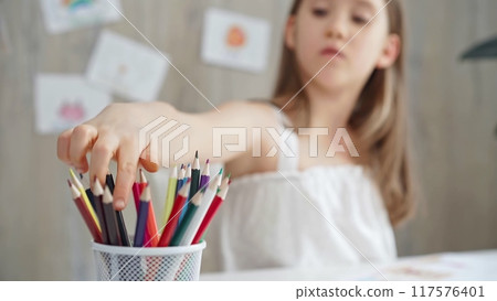 Close-up of a child's hand picking a pencil from a colorful set for a creative activity. Young girl choosing colored pencils Close-up of a child's hand picking a pencil from a colorful set for a creative activity. Young girl choosing colored pencils 117576401