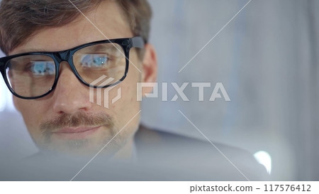 Businessman with glasses looking intently obscured partially by a translucent surface of laptop. Business concept Businessman with glasses looking intently obscured partially by a translucent surface of laptop. Business concept 117576412