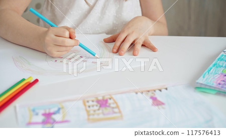Close-up of a child's hands coloring a drawing with bright pencils. Young girl engaging in colorful artistic drawing and coloring activity using pencils. Enhancing creativity. Imagination Close-up of a child's hands coloring a drawing with bright pencils. Young girl engaging in colorful artistic drawing and coloring activity using pencils. Enhancing creativity. Imagination 117576413