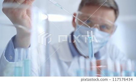 Man with safety glasses and blue mask is working with lab tubes using a pipette in a modern laboratory, close-up of researcher. Science and medicine 117576434