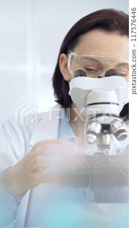 Scientist using microscope in laboratory. Focus on a woman in lab goggles analyzing samples with a microscope in a scientific setting. Science concept 117576446
