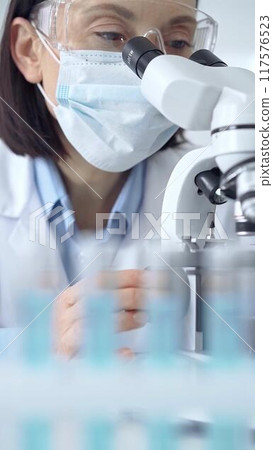 Female scientist using microscope in laboratory, portrait. Focus on a woman in lab goggles analyzing samples in a scientific setting 117576523