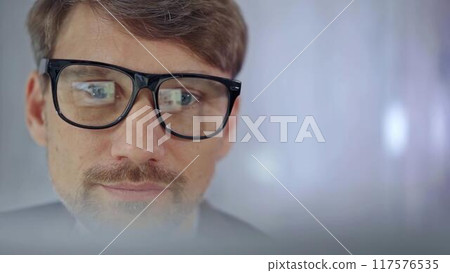 Businessman with glasses looking intently obscured partially by a translucent surface of laptop. Business concept Businessman with glasses looking intently obscured partially by a translucent surface of laptop. Business concept 117576535