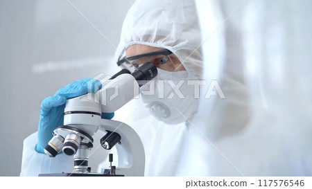 Scientist in ppe analyzing samples using a microscope in a laboratory setting. Close-up of a focused researcher in a lab coat mask and protective gear 117576546