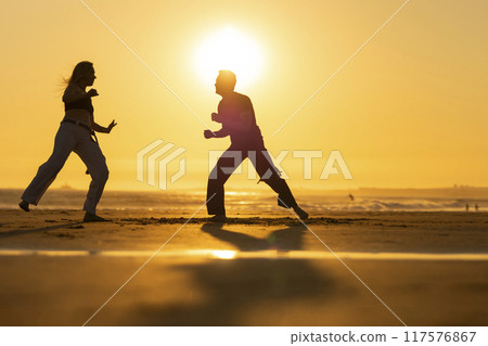 Couple practicing capoeira martial art at sunset on the beach Couple practicing capoeira martial art at sunset on the beach 117576867