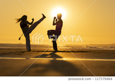Couple practicing capoeira martial arts on the beach at sunset Couple practicing capoeira martial arts on the beach at sunset 117576868