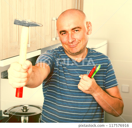 Ordinary man posing with a hammer in his hands Ordinary man posing with a hammer in his hands 117576916