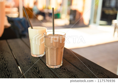 Two pink fruit milk cocktails in glasses with black tubes spiral pattern for milkshakes, cocktails, juices stand on table in street cafe. Bokeh background, backdrop 117576936