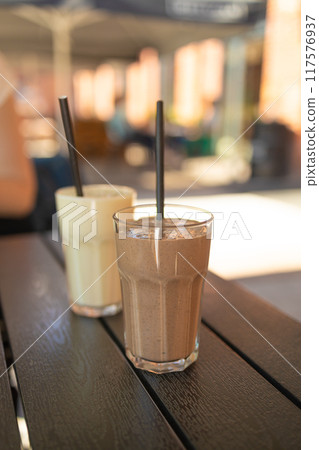 Two pink fruit milk cocktails in glasses with black tubes spiral pattern for milkshakes, cocktails, juices stand on table in street cafe. Bokeh background, backdrop 117576937