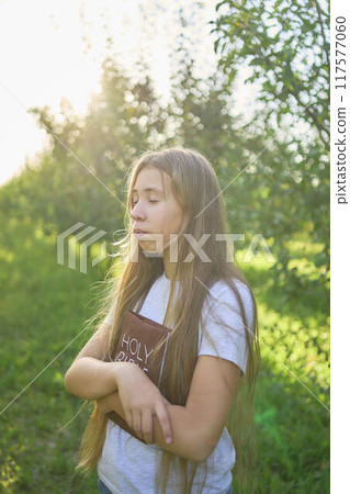 a teenage girl prays with a holy bible in a garden illuminated by light a teenage girl prays with a holy bible in a garden illuminated by light 117577060