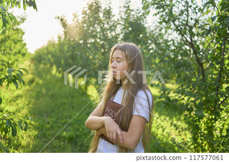 a teenage girl prays with a holy bible in a garden illuminated by light a teenage girl prays with a holy bible in a garden illuminated by light 117577061