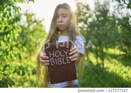 a teenage girl prays with a holy bible in a garden illuminated by light 117577147