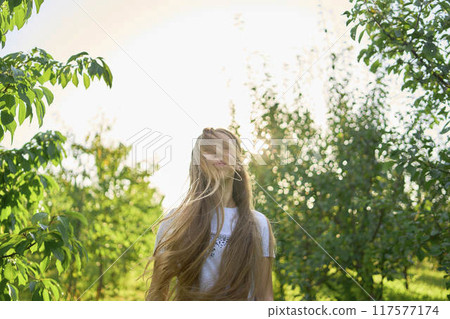 a portrait of a teenage girl with long blond hair in a sunlit garden 117577174