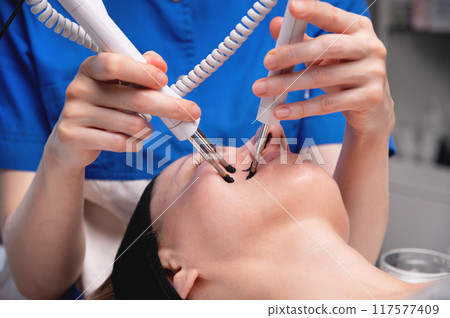 Ultrasonic facial treatment on ultrasound face machine. Woman taking electric lift massage spa salon. Stimulation muscles on professional equipment microcurrent therapy. New methods of rejuvenation Ultrasonic facial treatment on ultrasound face machine. Woman taking electric lift massage spa salon. Stimulation muscles on professional equipment microcurrent therapy. New methods of rejuvenation 117577409