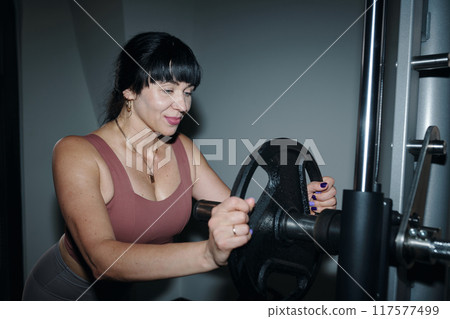 Woman Adding Weight On Barbell Before Training Woman Adding Weight On Barbell Before Training 117577499