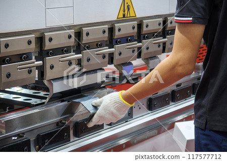 Close up the press brake bending machine operator hold the sheet metal parts with safety glove. 117577712