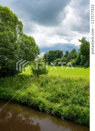 Creek, green meadows and trees at the German countryside around Bredenau, Lower Saxony, Germany 117577832