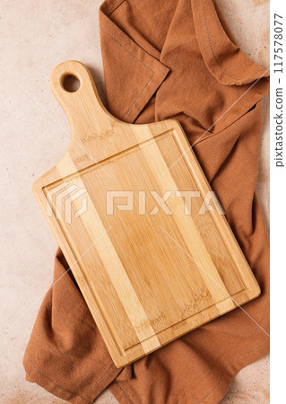 Cutting board, beige, unpainted, with a kitchen towel, on a beige background, top view, 117578077
