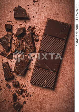 chocolate bar , for the manufacture of confectionery, broken, crumbled, on a brown background, top view, 117578088