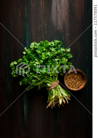bunch of fresh Cilantro, coriander seeds, on a dark wooden table, close-up, top view, no people. 117578091