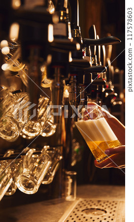 Bartender pouring lager foamy beer from tap into glass. Luxurious bar atmosphere Bartender pouring lager foamy beer from tap into glass. Luxurious bar atmosphere 117578603