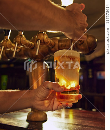 Close-up of male bartender hands pouring beer from tap into glass. Aesthetic of pub work and vintage luxurious settings Close-up of male bartender hands pouring beer from tap into glass. Aesthetic of pub work and vintage luxurious settings 117578614