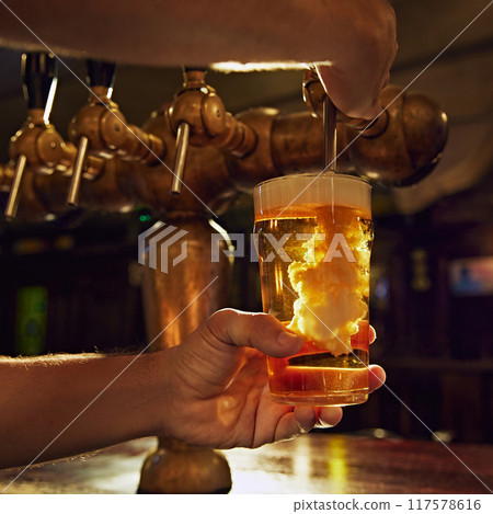 Close-up of male bartender hands pouring beer from tap into glass. Aesthetic of pub work and vintage luxurious settings Close-up of male bartender hands pouring beer from tap into glass. Aesthetic of pub work and vintage luxurious settings 117578616