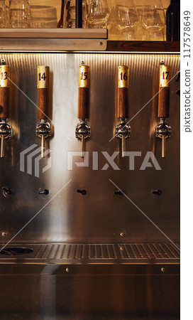Row of shiny metallic beer taps with numbered wooden handles, mounted on metallic wall. Modern bar equipment. Vertical image Row of shiny metallic beer taps with numbered wooden handles, mounted on metallic wall. Modern bar equipment. Vertical image 117578649