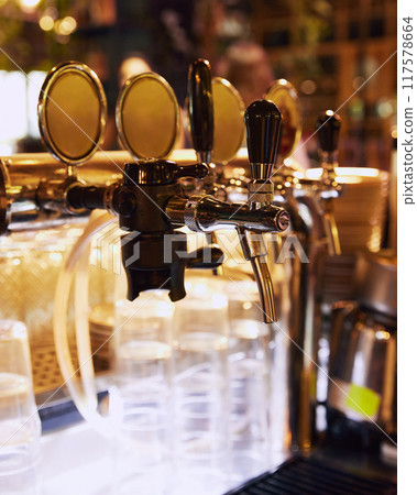 Close-up of multiple shiny golden beer taps with handles, set against blurred background with empty glasses. Luxurious bar Close-up of multiple shiny golden beer taps with handles, set against blurred background with empty glasses. Luxurious bar 117578664